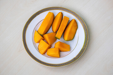 Ripe mango slices on a white plate on wooden background. 