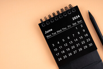 June 2024 Black spiral desktop calendar and wooden pencil.