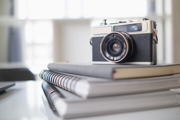 A vintage film camera sits on a table in an office and a book stands out in the background. A...