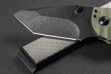 Man sharpens a knife using a whetstone on a dark table