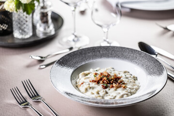 Halusky as traditional Slovak potato gnocchi with sheep cheese bryndza, fried bacon and chives served in a modern plate and on a festively laid restaurant table.