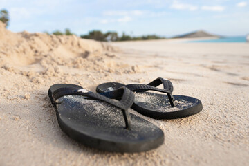 Black flip flops on white sand with sea background.