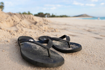 Black flip flops on white sand with sea background.