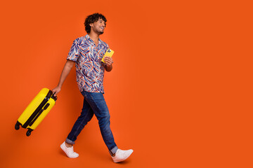 Full body photo of attractive young man hold suitcase device walking dressed stylish colorful clothes isolated on orange color background