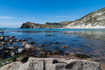 Lulworth Cove, Dorset, on a beautiful sunny April day with bright blue sky and sea, rocks with barnacles and chalky cliffs, a few small yachts
