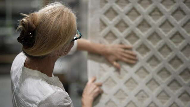 Back of mature woman hand touching carpet sample while looking through rugs for home redecorating project, in a hardware store.