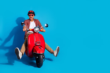 Full size photo of excited funny man dressed striped shirt trousers ride motorcycle near empty space isolated on blue color background