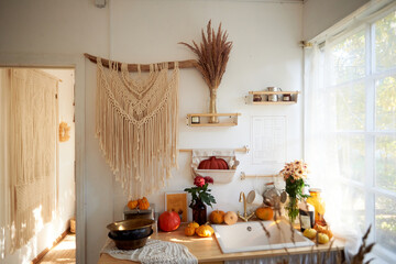 Cozy rustic kitchen with large window and lace curtains. On the wall hangs a large macrame, pumpkins, cereals