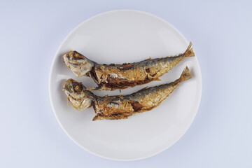 Fried mackerel on a white plate over a white background with studio lighting
