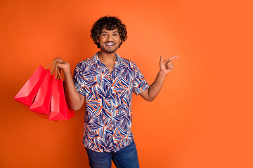 Photo portrait of attractive young man shopping bags point empty space dressed stylish colorful clothes isolated on orange color background