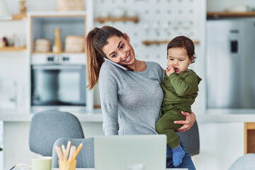 A smiling mother having a phone call and working from home while holding her toddler