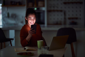 A happy young adult woman scrolling through her phone late at night and relaxing