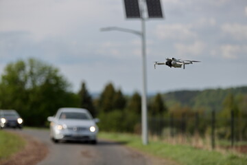 Dron w locie, w powietrzu, w tle panele słoneczne z latarnią uliczną, samochody osobowe na drodze. © Stanisław Błachowicz