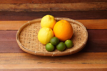 various types of oranges on a woven bamboo plate on a wooden background with studio lighting