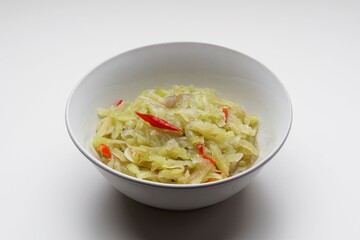 Stir-fried chayote vegetables with chopped garlic and red chilies in a white bowl on a white background