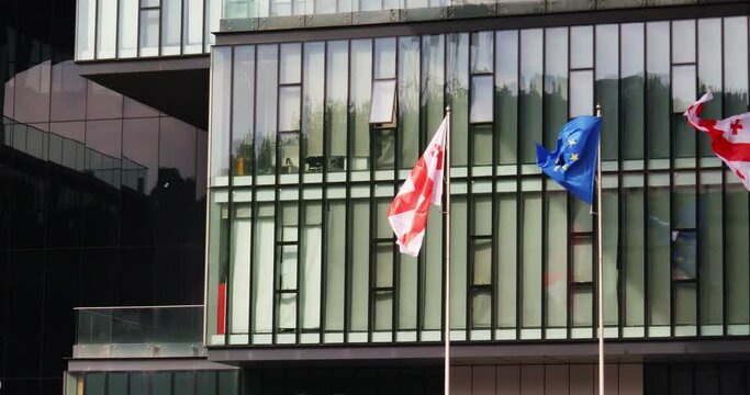 The EU and Georgian flags flutter against the background of the glass facade of the building. The path to mutually beneficial cooperation.