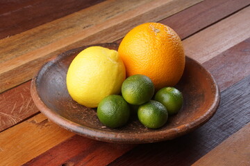 various types of oranges on a clay plate over a wooden background with studio lighting