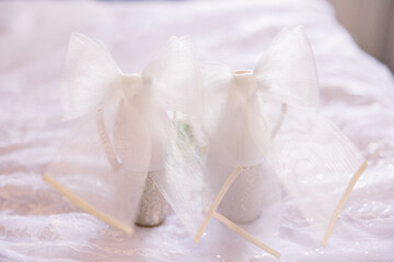 A gorgeous pair of white wedding shoes with see-through bow attached to the back of the shoes.