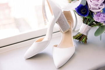 White wedding shoes styled on a window ledge next to the bridal bouquet. 