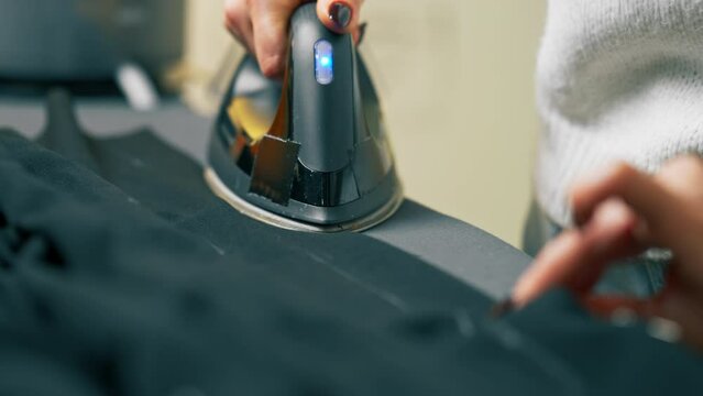 close-up in a sewing workshop seamstress irons black fabric for corrugation