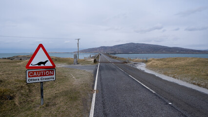 Scenic Outer Hebrides landscape with causeway over ocean, cyclist exploring the islands, and a road sign for otters crossing in Scotland UK