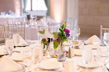 A close-up of a beautiful table set up for a wedding reception with a simple floral centerpiece and...