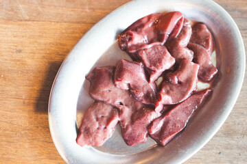 Pieces of raw pork liver on dish on wood table