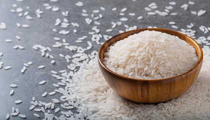 A wooden bowl filled with white rice, surrounded by scattered rice on a grey surface,  food, nutrition, agriculture. free copy space.