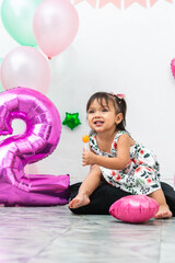 little latin brunette girl smiling and holding a candy in her hand while sitting, celebrating her...