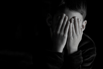 monochrome portrait of a child covering his face with his hands. Black background and copy space....
