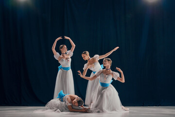 Four ballerinas, poised in white tutus with blue sashes, exhibit their refined ballet technique...