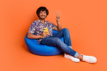 Full body photo of attractive young man bean bag device v-sign dressed stylish colorful clothes...