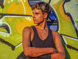 A young guy with streaked hair is photographed against a background of graffiti in a black T-shirt and looks to the side