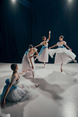 Four ballet dancers in flowing white costumes with blue ribbons, gracefully poised in different...