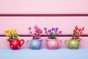 Small polka dot vases in different colors of blue, pink, green and red with colorful flowers on a blue surface and pink striped background.
