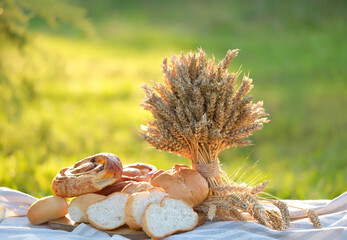 different baked breads and wheat ears bunch on table in garden close up, natural background. Bread...