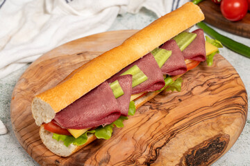 Smoked tongue sandwich on wood serving board. Sandwich made with smoked beef tongue, American salad, old cheddar cheese, tomato, cucumber and greens