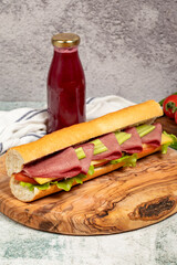 Smoked tongue sandwich on wood serving board. Sandwich made with smoked beef tongue, American salad, old cheddar cheese, tomato, cucumber and greens