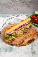Tuna sandwich on wood serving board. Sandwich made with tuna meat, special sauce, purple onion, pickles and greens