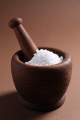 Natural salt in mortar and pestle on brown background, closeup