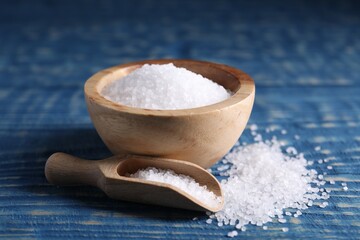 Natural salt in scoop and bowl on blue wooden table, closeup
