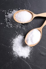 Natural salt and wooden spoons on black table, flat lay