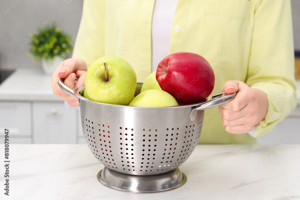 Wall mural woman holding colander with fresh apples at white marble table in kitchen, closeup