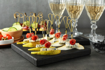 Tasty canapes with pears, blue cheese and prosciutto on grey table, closeup