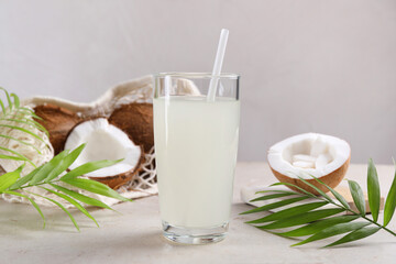 Glass of coconut water, palm leaves and nuts on light table