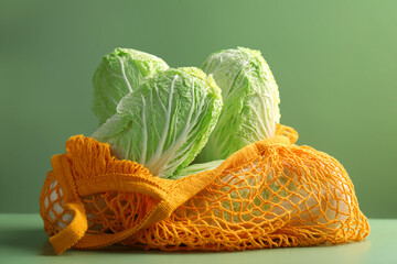 Fresh Chinese cabbages in string bag on green background, closeup