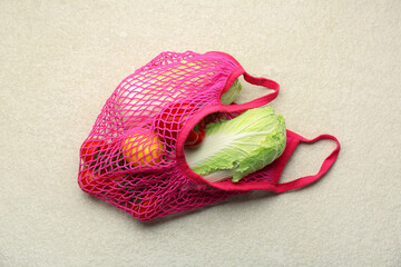 Fresh Chinese cabbage and other products in string bag on light textured table