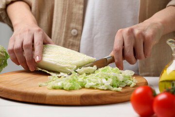 Woman cutting fresh chinese cabbage at white table, closeup