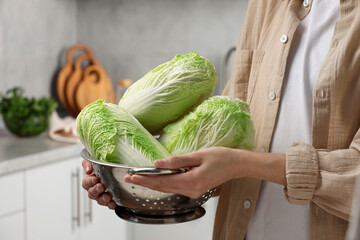 Woman holding fresh chinese cabbages in kitchen, closeup