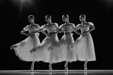 Young girls, ballerinas in white tutus with blue bows dancing in motion on stage. Monochrome photo...